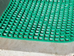 Green grid matting on a concrete surface, designed for drainage or stabilisation purposes.