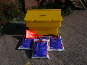 Yellow grit bin with de-icing salt bags and a bright orange scoop for winter road safety.