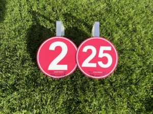 Two red and white distance markers on the grass, indicating rink measurements for a bowls game