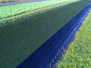 Artificial grass hedge by the roadside with a ditch channel