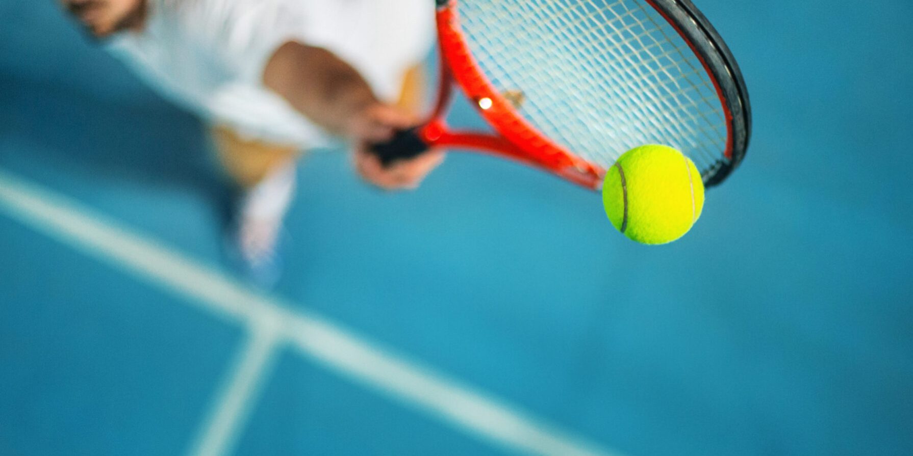 Tennis Essentials For Your Sports Club Close-up of a tennis player serving with a bright yellow tennis ball and a red racket on a blue court.